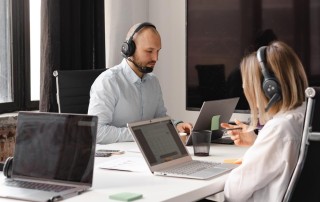 two colleagues working on laptops and headsets