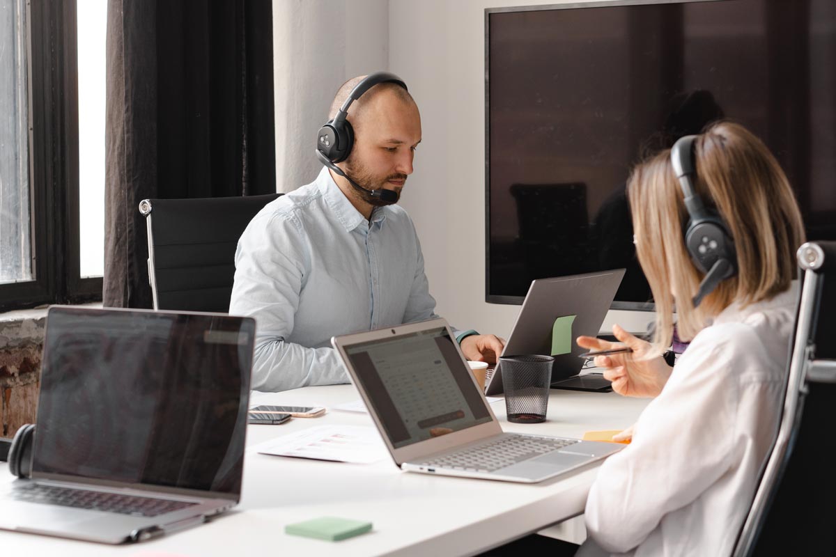 two colleagues working on laptops and headsets