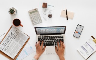 Woman on laptop with mobile phone and finance newspaper