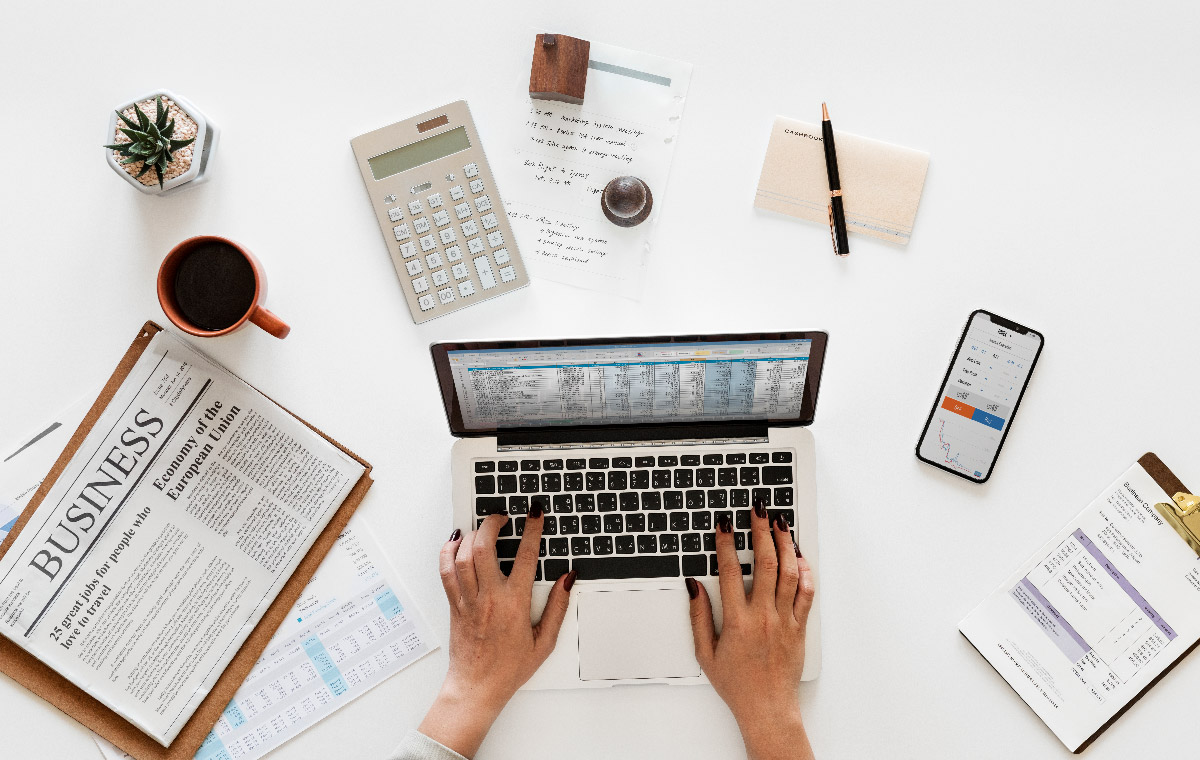 Woman on laptop with mobile phone and finance newspaper