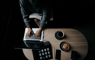 working on laptop at desk surrounded by other devices