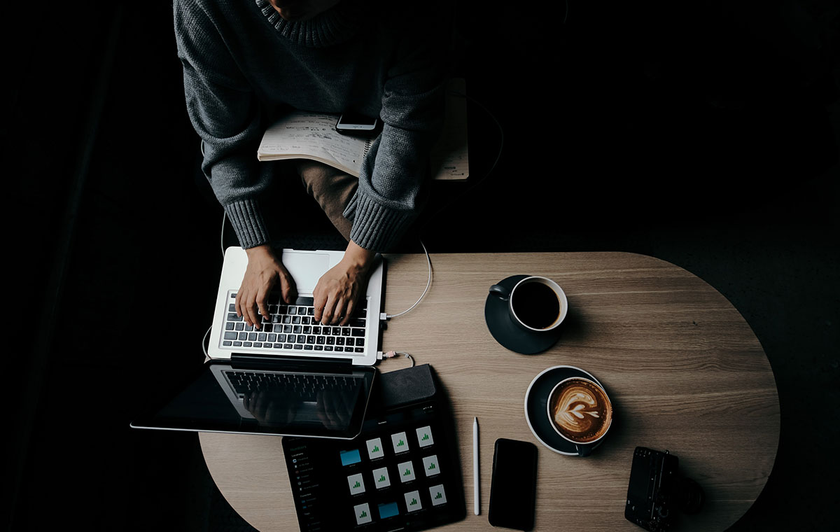 working on laptop at desk surrounded by other devices