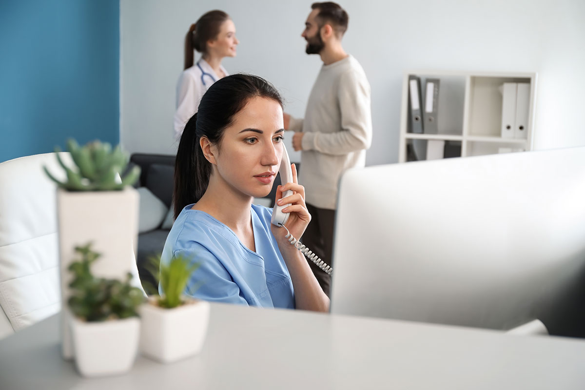 Female medical receptionist on phone will colleagues talking in background