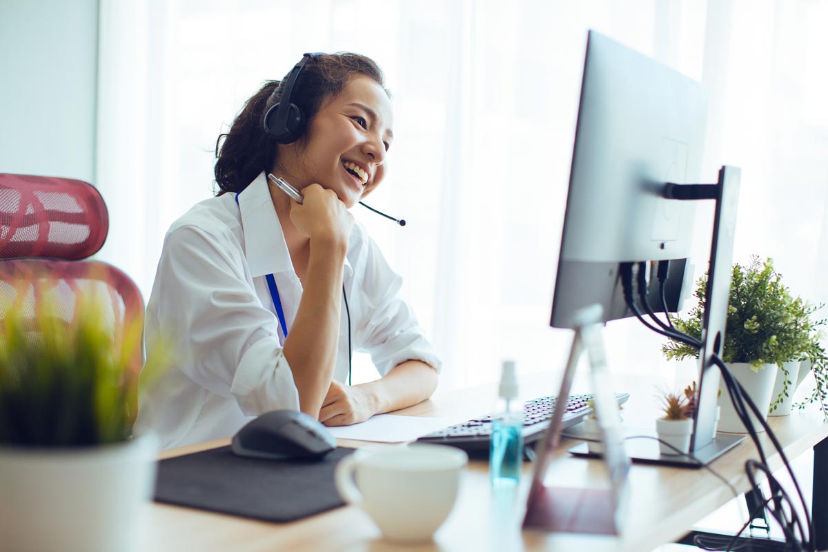 Girl with headset smiling and looking at desktop computer