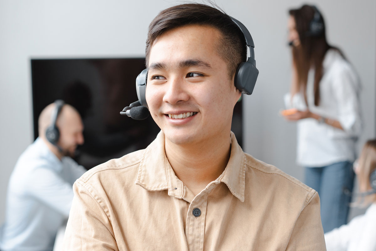 Young man in office wearing headset and smiling with colleagues in background